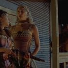 Ich kann keinen bestimmten Text im Bild erkennen. Zwei Frauen in Korsetts sind zu sehen, eine hält ein Gewehr. Eine Person zeigt auf etwas.