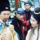 Eine historische Szene: Ein Mann mit traditioneller Kleidung betrachtet konzentriert ein Objekt, eine Frau schaut interessiert zu.