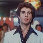 Leuchtende Schrift im Hintergrund, Mann in weißem Anzug, Menschenmenge und Discokugeln.