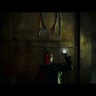 Eine Person leuchtet mit einer Taschenlampe an die Decke, wo lange, krallenartige Hände hängen. Die Szene wirkt düster.