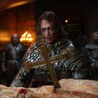 Ein Ritter in blutverschmierter Rüstung blickt ernst auf ein Kreuz. Im Hintergrund leuchten Kerzen.