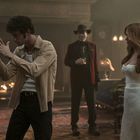 Drei Personen in eleganter Abendkleidung stehen in einem luxuriösen, warm beleuchteten Raum.