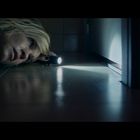 Eine Frau liegt am Boden und leuchtet mit einer Taschenlampe unter einer Tür durch.