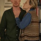 Ich kann den Text in diesem Bild nicht identifizieren, aber zwei Personen stehen eng beieinander in einem gemütlichen Raum.