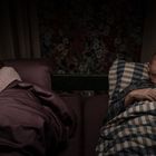 Zwei Personen liegen schweigend im Bett, abgewandt voneinander; sie wirken nachdenklich. Dunkles, gedämpftes Licht.