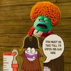 Eine grüne Zeichentrickfigur mit orangen Haaren steht hinter einem Schild, das besagt: "You must be this tall to enter big guy ride."