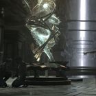 Ein spiralförmiges, leuchtendes Gebilde schwebt in einem futuristischen Raum. Zwei Personen knien davor; eine dritte steht.