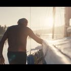 Boote im Sonnenuntergang, ein Mann geht am Wasser entlang. Text auf dem Boot: „RANGER“. Palmen im Hintergrund.