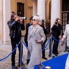 Mehrere Fotografen fotografieren zwei elegant gekleidete Frauen auf einem blauen Teppich vor einem historischen Gebäude.