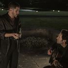 Zwei Männer, einer steht mit Bierflasche, der andere sitzt mit Gitarre. Hintergrund ist ein nächtlicher Garten.