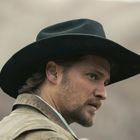 Ein Mann mit einem schwarzen Cowboyhut blickt nach rechts. Er trägt eine braune Jacke und hat einen Bart. Hintergrund unscharf.