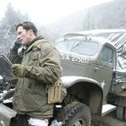S.A. 275057. Ein Mann in Winterkleidung telefoniert vor einem alten Militärfahrzeug im Schnee.