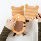 Papierkunstwerk von zwei tigergesichtigen Figuren; Hände positionieren die Köpfe.