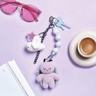 Eine rosa Sonnenbrille, zwei Schlüssel an einem Anhänger mit gehäkelten Figuren, Kaffee und ein offenes Buch auf hellem Hintergrund.