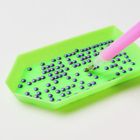 Ein grünes Tablett mit vielen kleinen, lila Perlen und ein pinkfarbener Stift, der eine Perle aufnimmt.