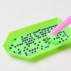 Grünes Tablett mit lila Perlen. Ein pinker Stift scheint Perlen aufzunehmen.