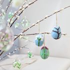 Zweige mit handgefertigten Filz- und Glaseiern, geschmückt mit Blumenmustern und zarten Zweigen in einem gemütlichen Wohnzimmer.