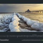 Kalendermonat: Dezember; Tagelang, frostbedeckte Mole im Meer. Rechts Holzsteg mit Gebäude, sanftes Licht.