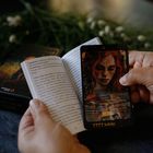 Ein Buch offenbart Text zu "VIER DER KELCHE", eine Karte mit rothaariger Frau darüber gehalten.