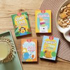 Vier Kartenspiele: "Coco Loco", "Eisdiele", "Krake im Stall", "Tumult im Teich" von Pattloch. Holzuntergrund mit Snacks.