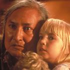 Zwei Personen: Eine ältere Person mit langen Haaren und eine junge, blonde Person. Beide schauen ernst und sind nah beieinander.