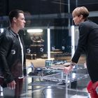 Zwei Personen in einem Raum getrennt durch Glas, links steht ein Mann in schwarzer Jacke, rechts eine Frau in rotem Ledermantel.