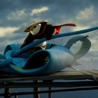 Illustration: Ein Panda in einem roten Umhang und Strohhut reitet auf einer blauen, fliegenden Kreatur über einen Steg.