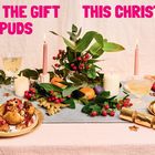 „GIVE THE GIFT OF SPUDS THIS CHRISTMAS“. Ein festlich gedeckter Tisch mit Kerzen, blättrigen Zweigen und Tellern mit Kartoffeln.