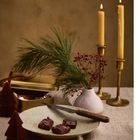 Kerzen und Schokolade dekorativ arrangiert, mit Tannenzweigen und kleinen roten Beeren in einer Vase.