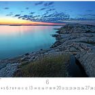 Küste in der Mitternachtssonne. Eine felsige Küste mit ruhigem Wasser unter einem farbenfrohen Sonnenuntergangshimmel.