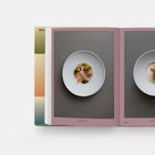 Rechts oben: "WINTER". Zwei Teller mit kunstvoll angerichteten Speisen auf grauem Hintergrund. Offenes Buch mit rosa Seitenrahmen.