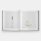 Links "Eau d’Issey", rechts rundes Parfüm. Buch offen auf heller Seite.