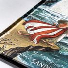 Text: "SANDR". Illustration eines Mäuschens im roten Umhang steht auf einer Klippe am Meer, dazu Pflanzen und Wasser.