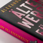 „Älterwerden für Anfänger“ in großen, glänzend pinken Buchstaben auf schwarzem Hintergrund.