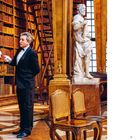 Zahl 99 unten rechts. Bibliothek mit Holzregalen, einer Statue, einem Mann im Anzug und zwei Stühlen.
