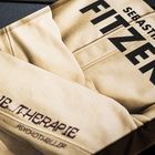 "Sebastian Fitzek", "Die Therapie", "Psychothriller". Beige Stoffstruktur im Hintergrund.