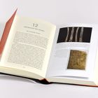 Ein aufgeschlagenes Buch zeigt den Titel "Der Bischof des Geldes" und enthält Abbildungen historischer Artefakte.