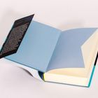 Ein aufgeschlagenes Buch mit hellblauem Einband und einem Umschlag mit Text auf der Innenseite.