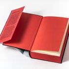 Ein geöffnetes Buch mit rotem Einband und rotem Vorsatzblatt. Text auf dem Schutzumschlag ist lesbar.