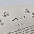 Text: "KAPITEL 29 LIORA". Blumenillustrationen umgeben den Titel. Darunter beginnt Text in einem Buch.