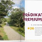 „PRÄDIKAT PREMIUM“ in großer lilafarbener Schrift, darunter „… auf der Husby Klitplantage Route #26“. Links ein Waldweg.