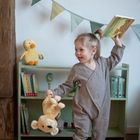 Ein Kind hält ein Buch mit dem Titel "Kleine Eule ganz allein". Es trägt einen karierten Anzug und tanzt mit einem Stofftier.