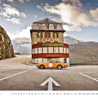 Hotel "Gletscher Restaurant Belvedere" vor Bergen, orangefarbenes Auto im Vordergrund auf Straße.