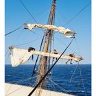 06

Zwei Personen arbeiten auf Segeln eines Schiffs in blauer See. Klarer Himmel. Segelmast mit mehreren Taue.