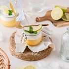 Kleine Gläser mit Sahne, Limettenspalten und Minze, dekoriert mit Cocktail-Schirmchen, serviert auf einem runden Jutepad.