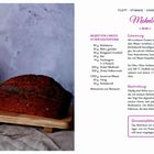 Rezept für Mohnbrot. Zutaten und Zubereitung angegeben. Bild zeigt ein gebackenes Brot auf Holzbrett, Mohn daneben.