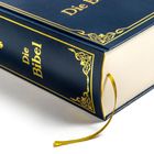 "Die Bibel" auf dem Buchrücken in Gold und ein goldenes Kreuz. Dunkelblaues Buch mit Lesezeichen.
