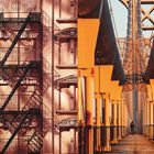 Es sind keine lesbaren Texte vorhanden. Links Feuerleiter an Backsteinfassade, rechts Brückenstruktur mit Mensch auf der Brücke.