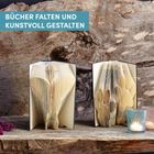Text: "BÜCHER FALTEN UND KUNSTVOLL GESTALTEN". Zwei kunstvoll gefaltete Bücher auf Holzhintergrund; Kerzen im Vordergrund.