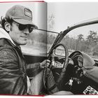 Der Text auf der Mütze zeigt "Chevrolet." Eine Person fährt ein Cabriolet, trägt Lederjacke und Sonnenbrille.